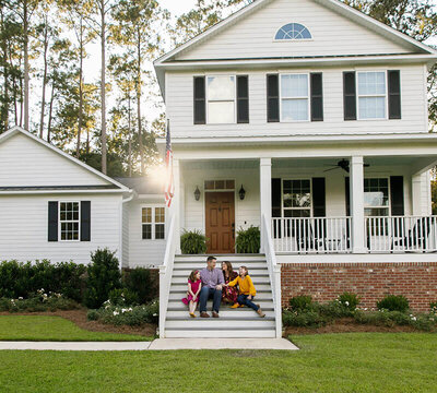 Happy family sitting on the steps in front of a beautiful home with white and black exterior paint